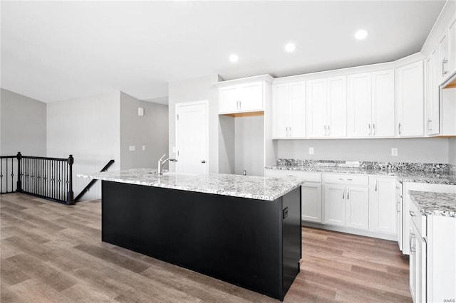 kitchen featuring light stone counters, an island with sink, white cabinetry, and light hardwood / wood-style flooring