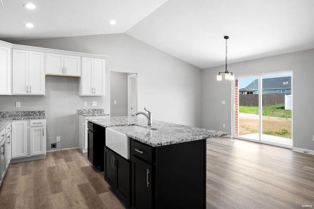 kitchen with vaulted ceiling, decorative light fixtures, light stone counters, light wood-type flooring, and white cabinets