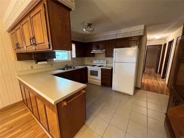 kitchen featuring light wood-type flooring, white appliances, sink, kitchen peninsula, and a textured ceiling