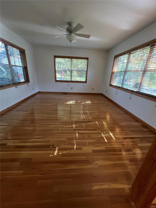 empty room featuring dark wood-type flooring, a healthy amount of sunlight, and ceiling fan