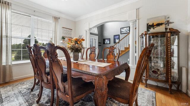 dining space featuring arched walkways, light wood-style floors, ornamental molding, stairs, and ornate columns