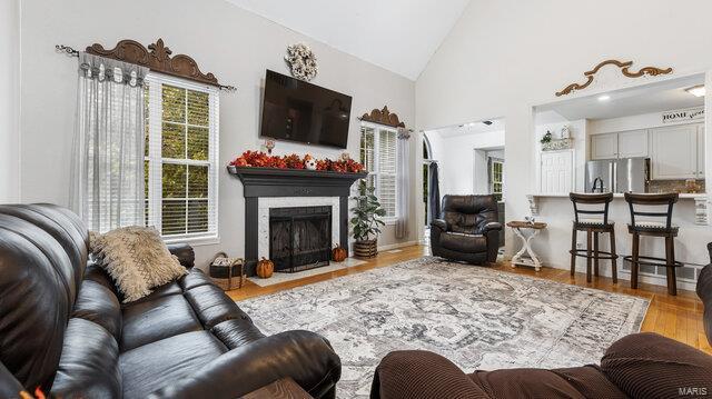 living area with a fireplace with flush hearth, high vaulted ceiling, and wood finished floors