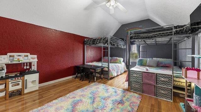 bedroom with lofted ceiling, a ceiling fan, wood finished floors, and a textured wall