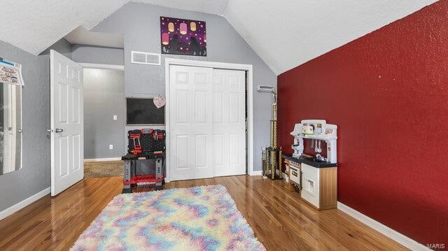 bedroom featuring lofted ceiling, wood finished floors, visible vents, baseboards, and a closet