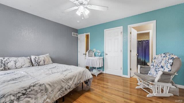 bedroom with baseboards, visible vents, a ceiling fan, wood finished floors, and a walk in closet