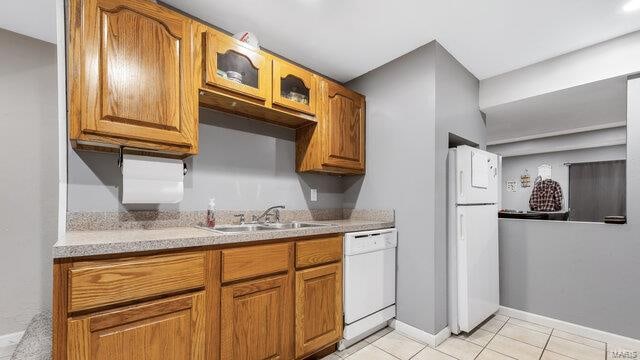 kitchen featuring white appliances, brown cabinetry, glass insert cabinets, a sink, and light tile patterned flooring