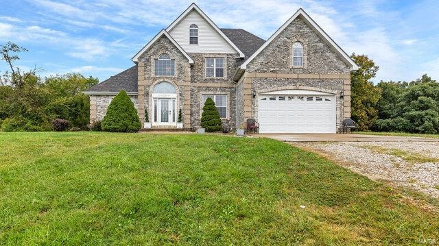 view of front facade featuring a garage, a front yard, gravel driveway, and stone siding