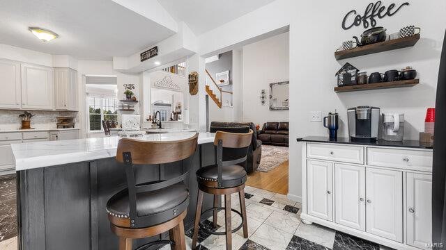 kitchen featuring a breakfast bar area, open shelves, decorative backsplash, white cabinetry, and a sink