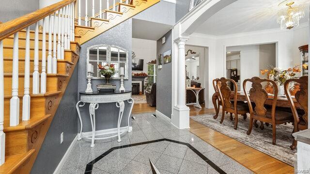 interior space featuring crown molding, decorative columns, light hardwood / wood-style flooring, and a chandelier