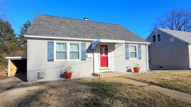 bungalow-style home with a shingled roof, driveway, a carport, and a front lawn