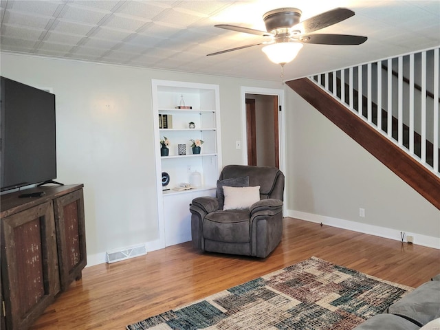 living area featuring wood finished floors, visible vents, baseboards, built in features, and stairway