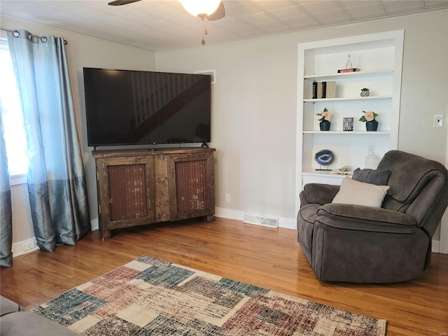 living room featuring visible vents, built in features, ceiling fan, wood finished floors, and crown molding