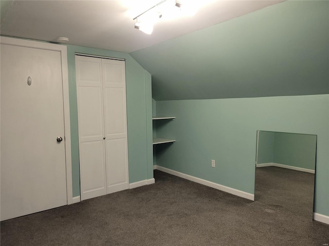 interior space featuring dark colored carpet, vaulted ceiling, and baseboards