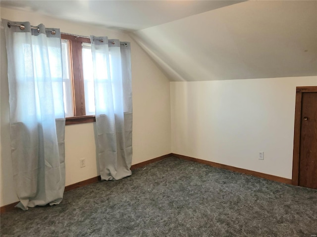 additional living space with lofted ceiling, dark colored carpet, and baseboards