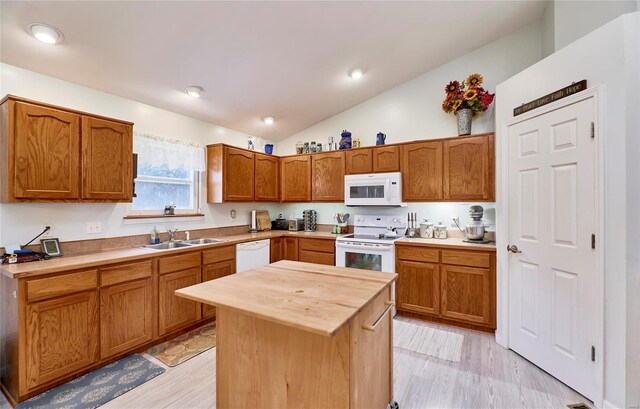 kitchen with vaulted ceiling, white appliances, a kitchen island, light wood-type flooring, and sink