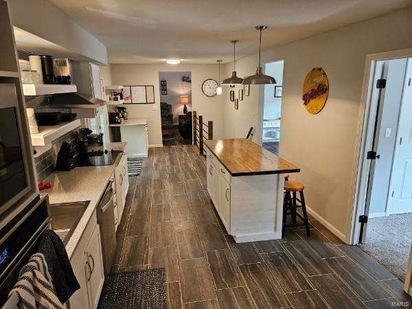 kitchen with hanging light fixtures, a kitchen bar, white cabinetry, dark wood-type flooring, and a kitchen island