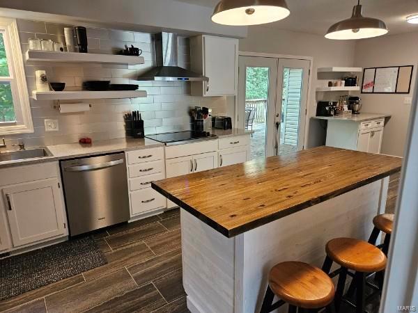 kitchen featuring butcher block counters, a kitchen bar, dishwasher, wall chimney exhaust hood, and white cabinets