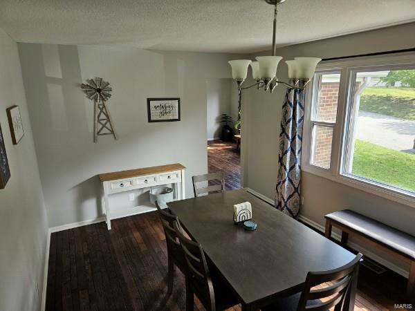 dining space featuring dark wood-type flooring, an inviting chandelier, and a textured ceiling