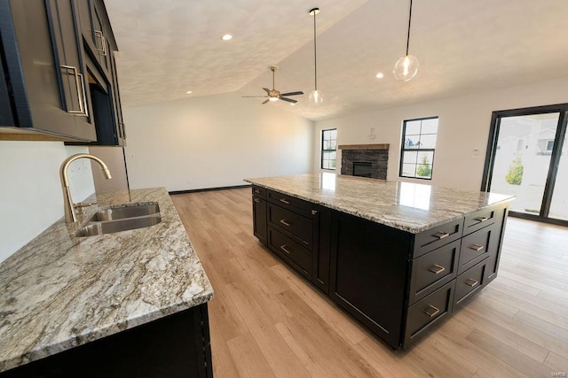 kitchen with light wood-type flooring, sink, ceiling fan, a stone fireplace, and lofted ceiling