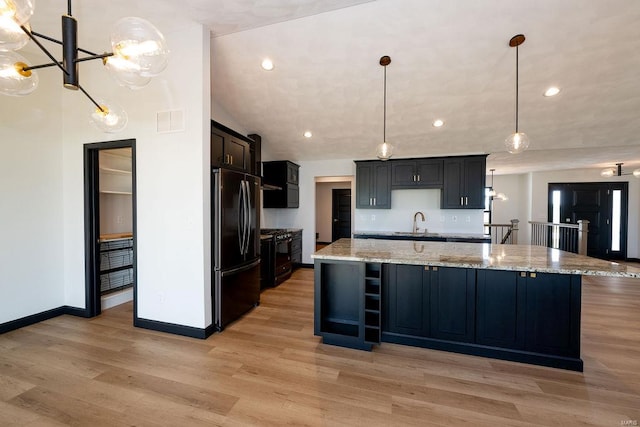 kitchen with pendant lighting, stainless steel refrigerator, light stone counters, a large island, and light wood-type flooring