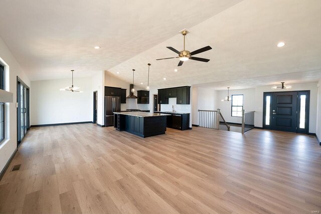 unfurnished living room featuring ceiling fan with notable chandelier, light wood-type flooring, lofted ceiling, and sink