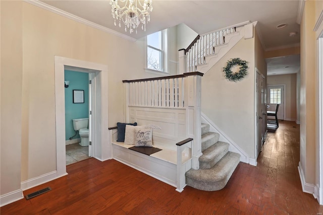 stairway with hardwood / wood-style flooring, a healthy amount of sunlight, crown molding, and an inviting chandelier