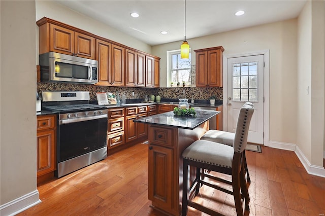 kitchen with pendant lighting, light wood-type flooring, appliances with stainless steel finishes, a kitchen island, and a breakfast bar area