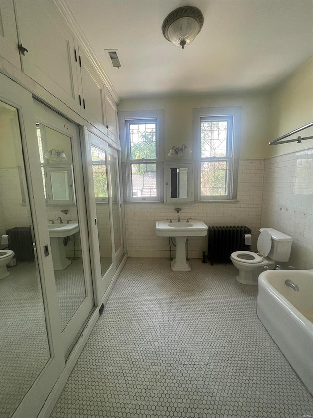 bathroom featuring tile walls, a bidet, toilet, and radiator