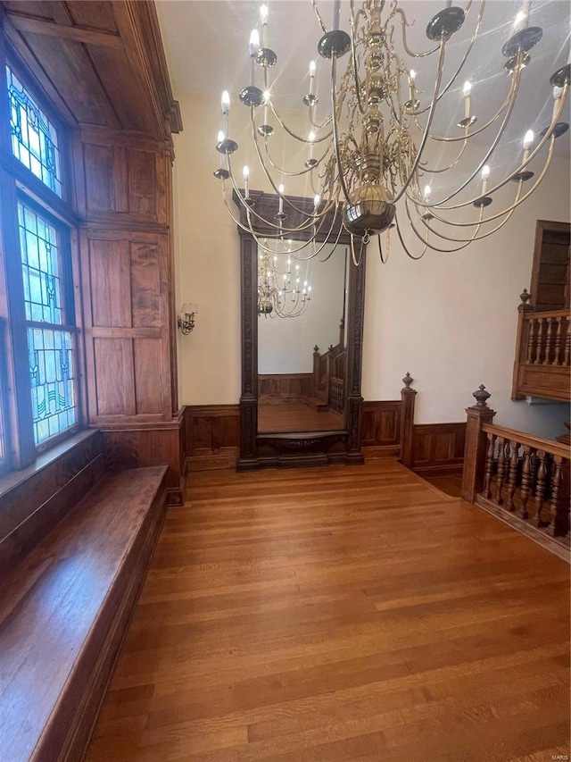 unfurnished dining area with hardwood / wood-style floors, wood walls, and an inviting chandelier