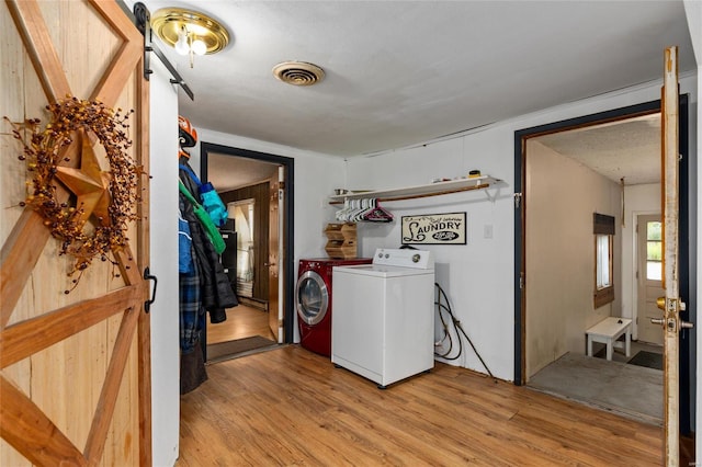 clothes washing area with washer and clothes dryer, a barn door, and light hardwood / wood-style floors