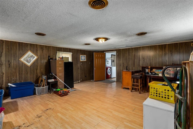 interior space with light wood-type flooring, wood walls, washer / dryer, and a textured ceiling