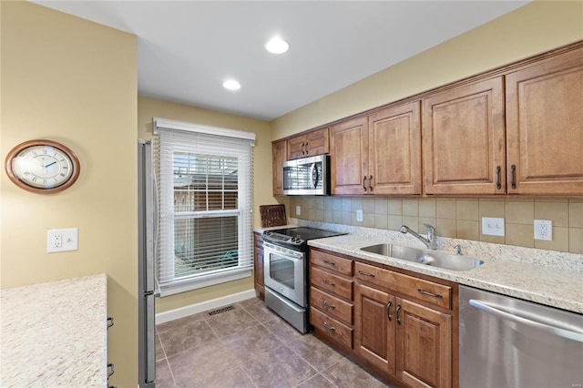 kitchen featuring dark tile patterned flooring, light stone countertops, sink, stainless steel appliances, and decorative backsplash