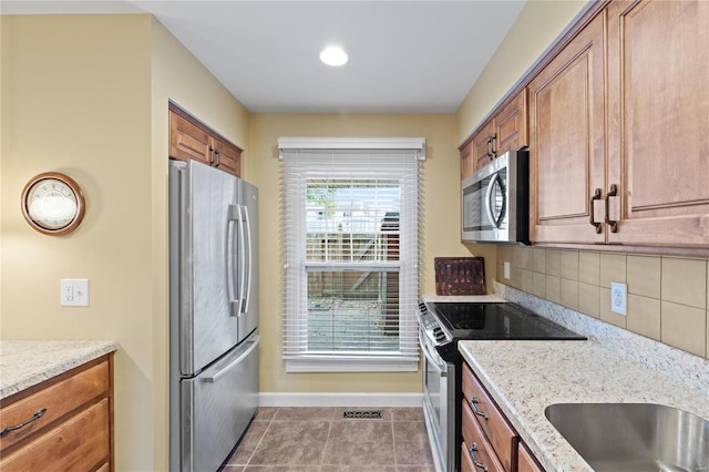 kitchen with light stone countertops, stainless steel appliances, light tile patterned floors, and backsplash