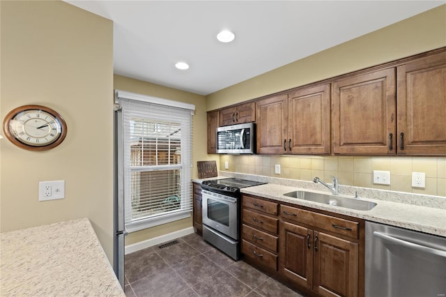 kitchen with dark tile patterned floors, stainless steel appliances, sink, light stone countertops, and tasteful backsplash