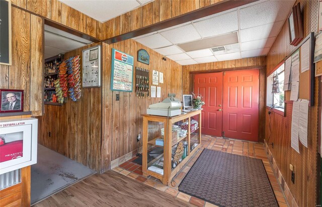 foyer with wood walls, wood-type flooring, and a paneled ceiling