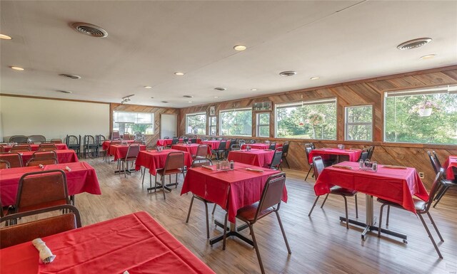 dining area featuring light wood-type flooring, wooden walls, and a healthy amount of sunlight