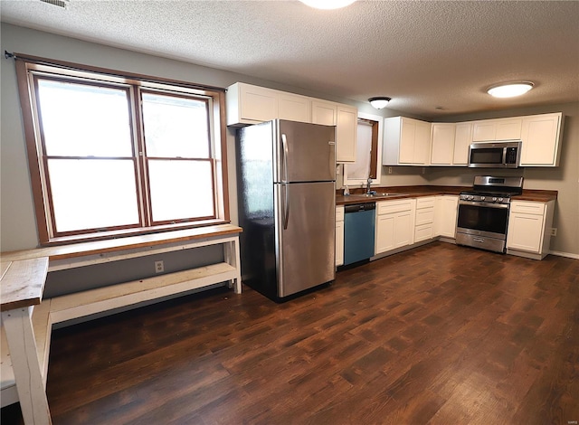 kitchen featuring a textured ceiling, appliances with stainless steel finishes, dark hardwood / wood-style flooring, and white cabinetry