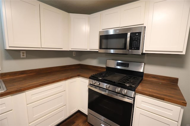 kitchen with appliances with stainless steel finishes, white cabinetry, dark hardwood / wood-style floors, and wooden counters