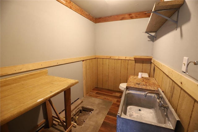 bathroom with hardwood / wood-style floors, wood walls, toilet, and sink