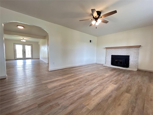 unfurnished living room with french doors, ceiling fan, hardwood / wood-style flooring, and a brick fireplace