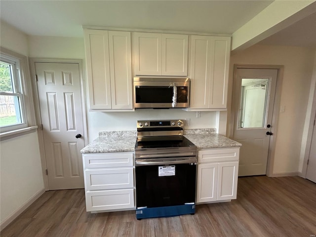 kitchen with stainless steel appliances, hardwood / wood-style floors, white cabinetry, and light stone countertops