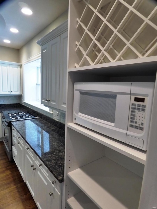 kitchen with dark wood-type flooring, dark stone countertops, stainless steel range, and white cabinetry