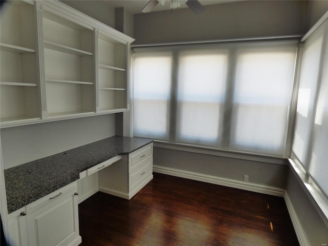 unfurnished office featuring built in desk, ceiling fan, and dark hardwood / wood-style floors