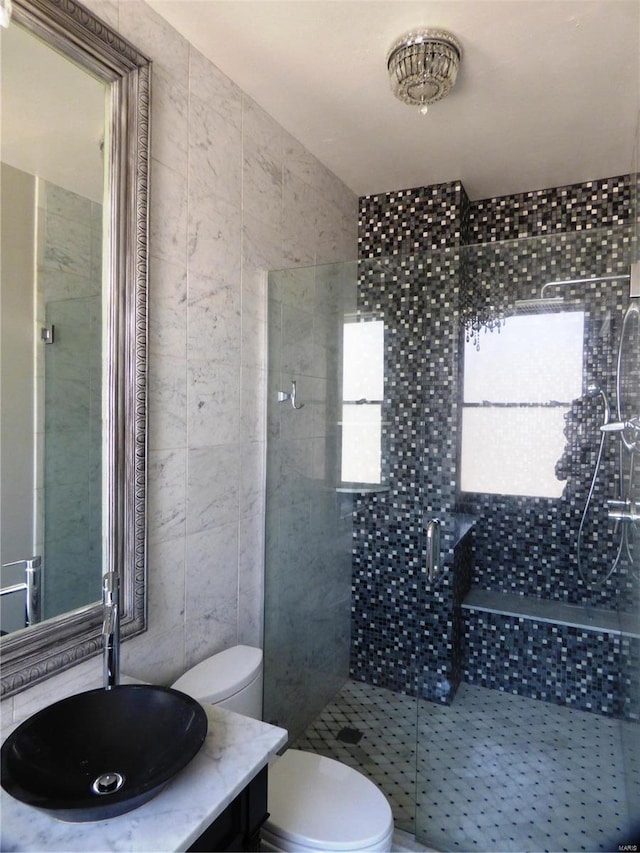 bathroom featuring tile walls, walk in shower, toilet, and vanity