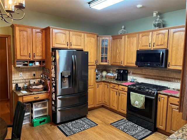 kitchen with light wood-type flooring, black appliances, decorative backsplash, and light stone countertops