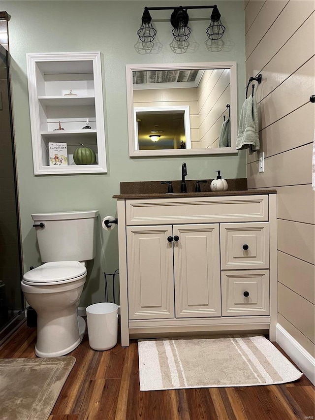 bathroom with wood walls, wood-type flooring, vanity, and toilet