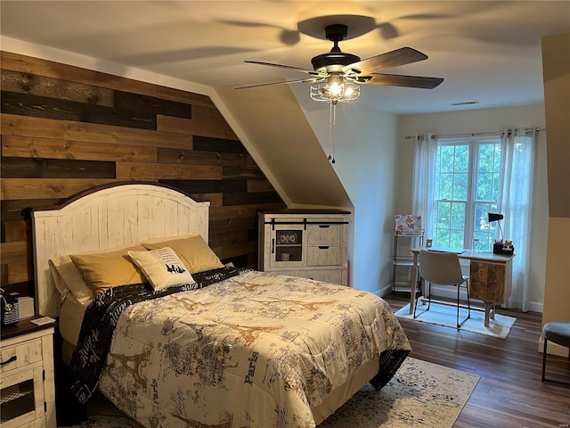 bedroom featuring ceiling fan, wooden walls, and dark hardwood / wood-style floors