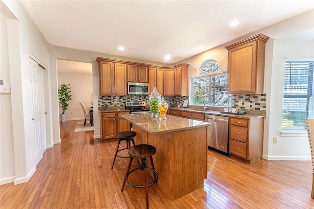 kitchen featuring a kitchen bar, appliances with stainless steel finishes, light stone counters, a center island, and light hardwood / wood-style floors