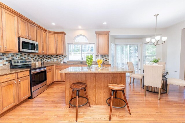 kitchen with tasteful backsplash, light stone counters, stainless steel appliances, sink, and a notable chandelier