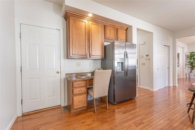 kitchen with stainless steel fridge, light hardwood / wood-style flooring, and dark stone counters